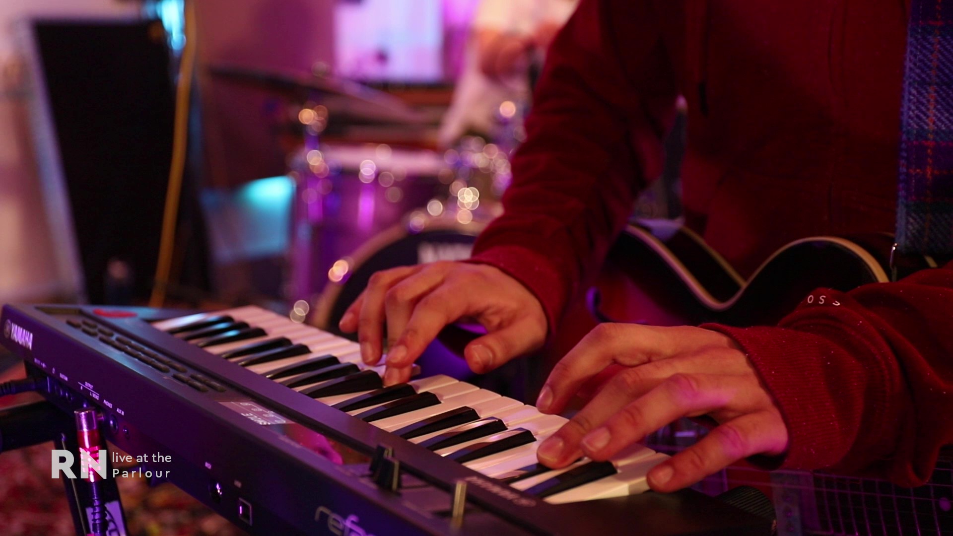 Man playing keyboard with electric guitar on his lap.